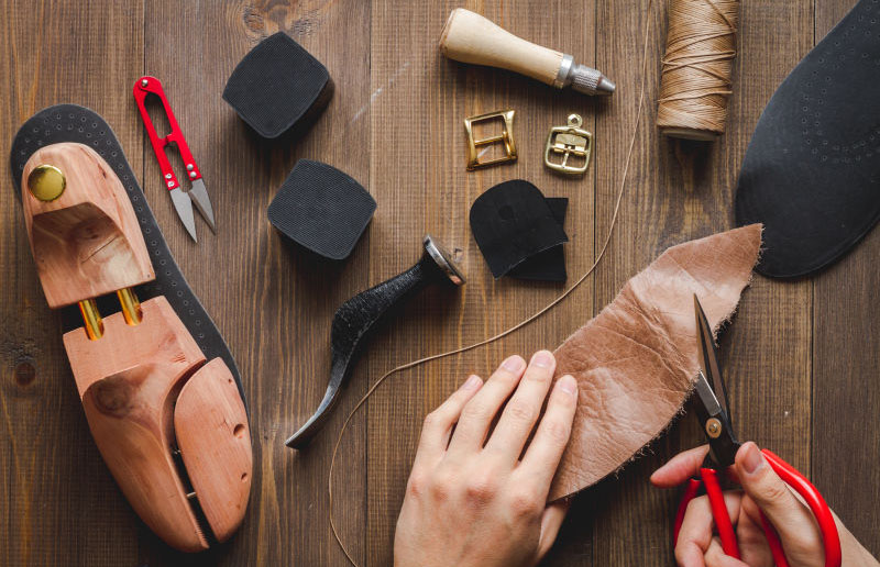 cobbler tools in workshop on dark background top view with hands
